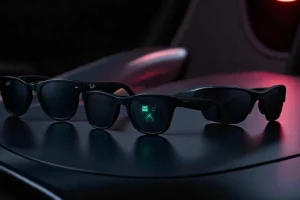 Trois modèles de lunettes connectées Meta 2025 posées sur une surface sombre : Ray-Ban Meta Gen 2 au style Wayfarer, Meta Ray-Ban Display avec affichage holographique vert dans le verre droit, et Oakley Meta Vanguard au design sportif noir.